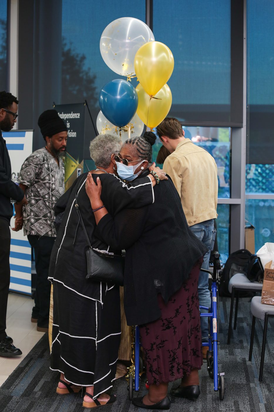 Two guests share a long hug under gold and blue balloons at the reception.