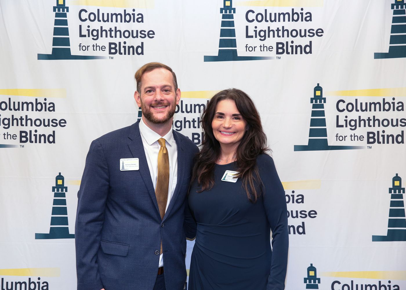 Rebecca Liko and Zachary Brewer smile together in front of a Columbia Lighthouse for the Blind backdrop.