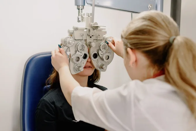 An eye-care specialist adjusts a phoropter positioned in front of a seated patient to measure her vision during a low-vision eye examination.