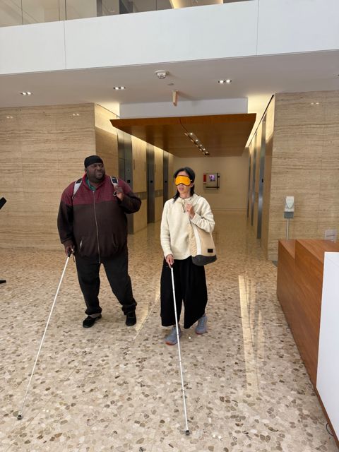 In the lobby of CLB&rsquo;s office building, Antonio Williams and a blindfolded Alisa Tang walk toward the exit, both with white canes.
