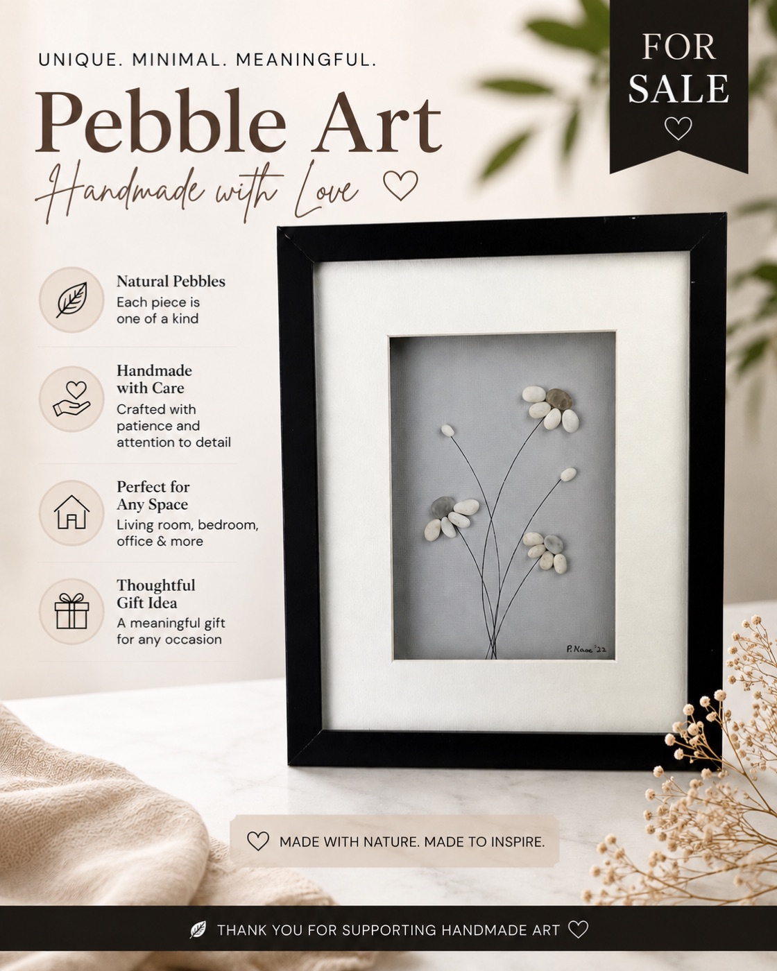 Framed pebble art of white daisy flowers on thin stems against a soft gray background.