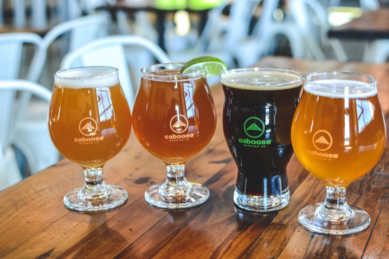 Four glasses of different Caboose Brewing beers arranged on a wooden outdoor table.