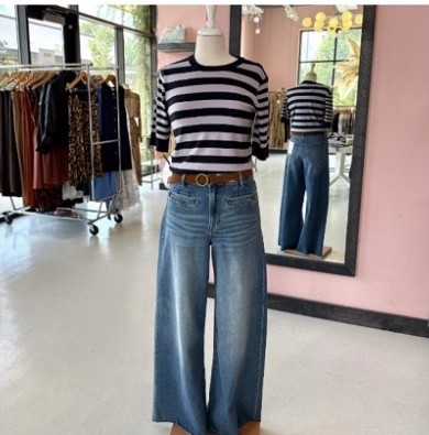 Inside the Jurisdiction Clothing boutique, a mannequin wearing a striped top and wide-leg jeans stands in front of a mirror, with clothing racks along pink walls.